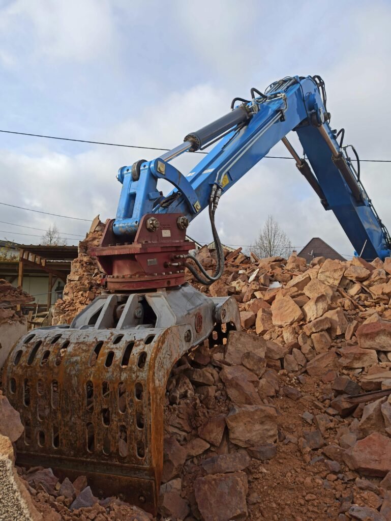 A blue excavator clearing rubble at a construction site under a cloudy sky.